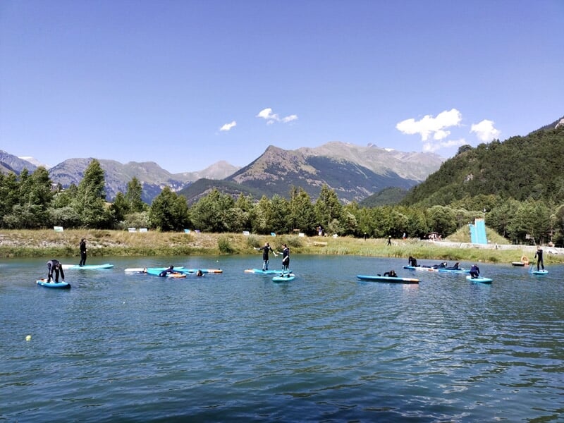Groupe de personnes pratiquant le stand-up paddle sur un lac entouré de montagnes et de verdure.