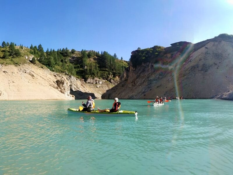Personnes en canoë et kayak pagayant sur un lac turquoise entouré de montagnes rocheuses.