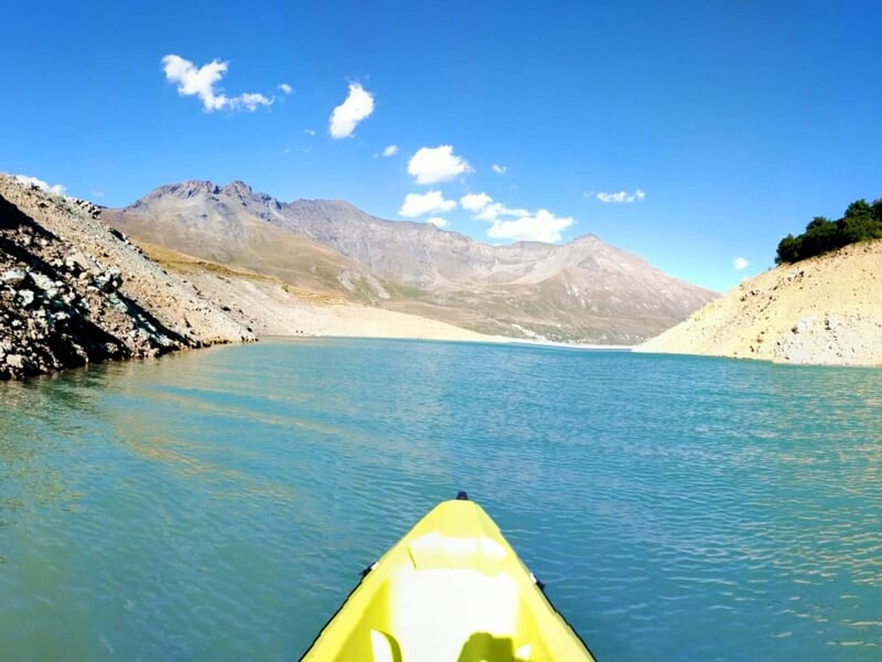 Groupe de personnes en canoë-kayak sur un lac de montagne aux eaux calmes et claires.