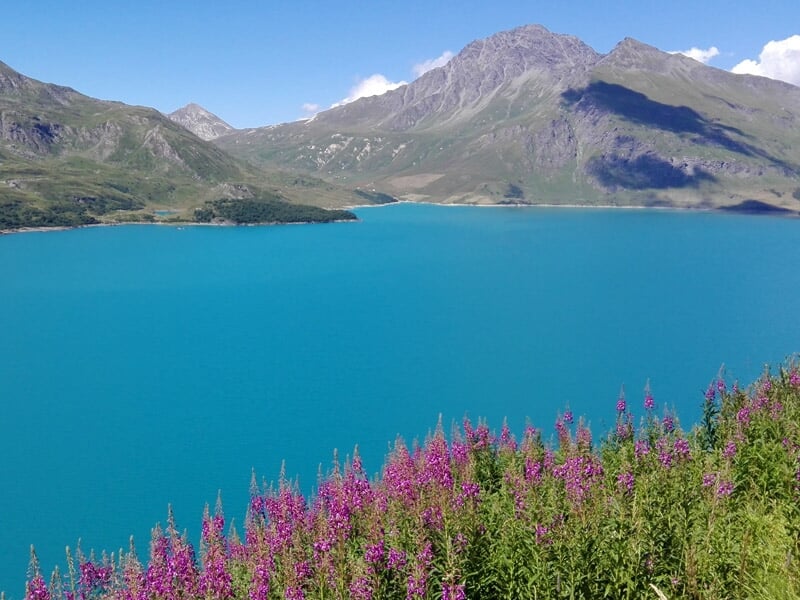 Personnes en canoë-kayak pagayant sur un lac de montagne avec forêt et montagnes en arrière-plan.