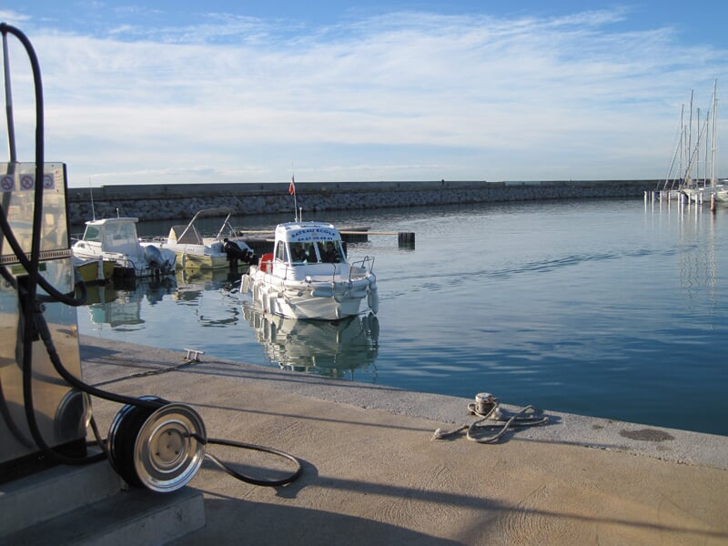 Vue d'un petit bateau blanc amarré dans un port calme avec un ciel bleu et un quai en béton au premier plan.