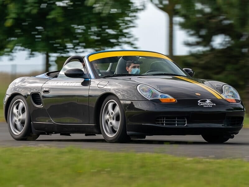 Porsche Boxster noire sur un circuit, avec un enfant au volant, portant un masque chirurgical