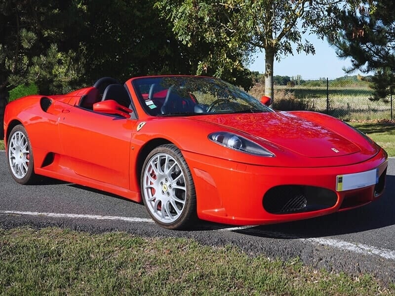 Une Ferrari F430 Spider rouge, un cabriolet de luxe avec des lignes élégantes, stationné sur une route bordée d'arbres.
