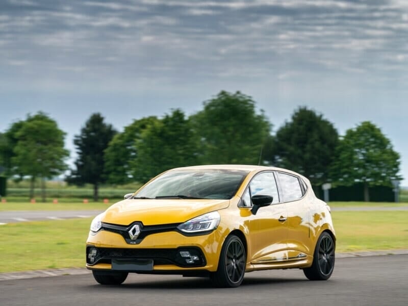 La première image montre une voiture Renault Clio RS jaune, une compacte sportive sur une piste entourée de verdure. Son design agressif et ses jantes noires renforcent son allure dynamique.