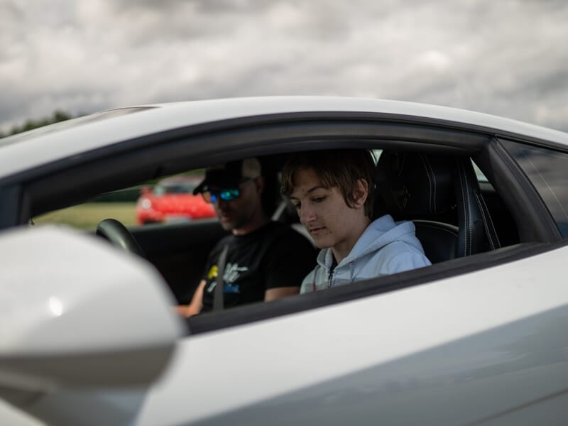 Un enfant assis dans une voiture de sport blanche avec un instructeur à ses côtés lors d'un stage de pilotage.