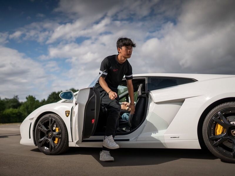 Un adolescent sort d'une voiture blanche de sport sur un circuit, prêt à participer à une activité de pilotage.