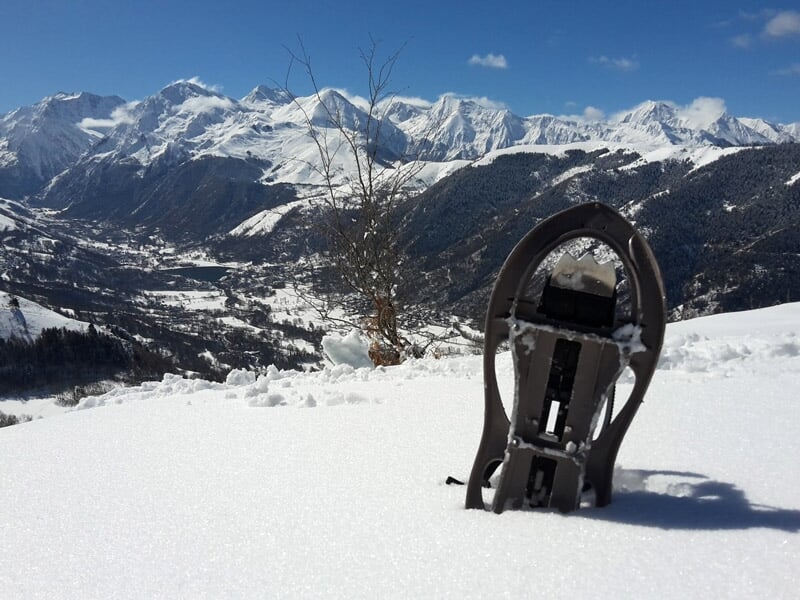 Raquette plantée dans la neige avec vue sur les montagnes enneigées sous un ciel bleu clair à Arreau.