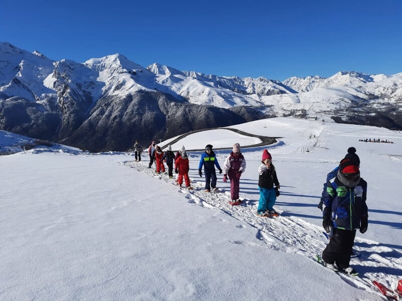 Groupe d'enfants en file indienne marchant sur la neige sous un ciel bleu dans les montagnes.