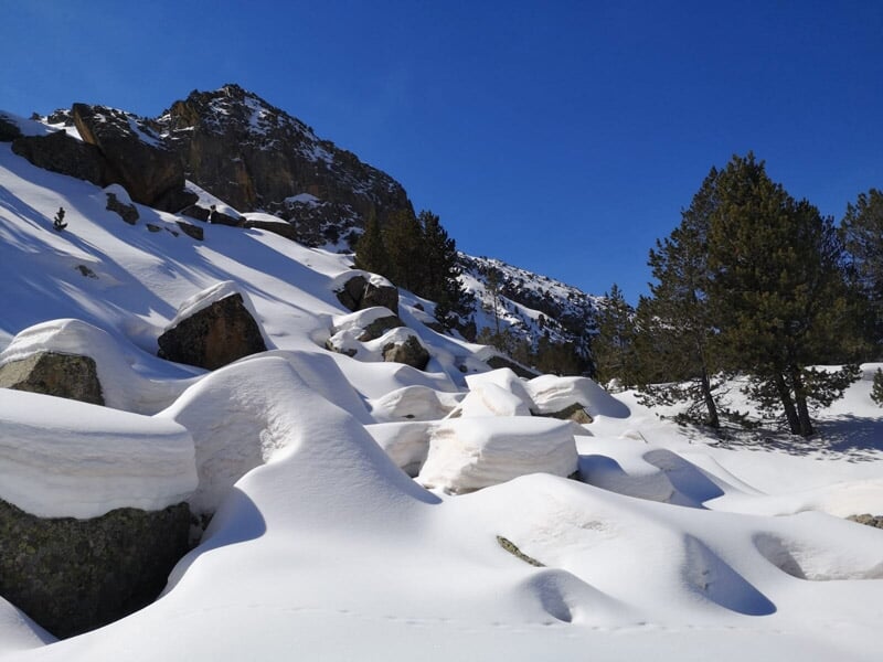 Paysage montagneux avec rochers et arbres partiellement recouverts de neige sous un ciel bleu.