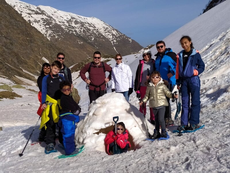 Groupe de randonneurs posant devant un igloo dans une vallée enneigée entourée de montagnes.