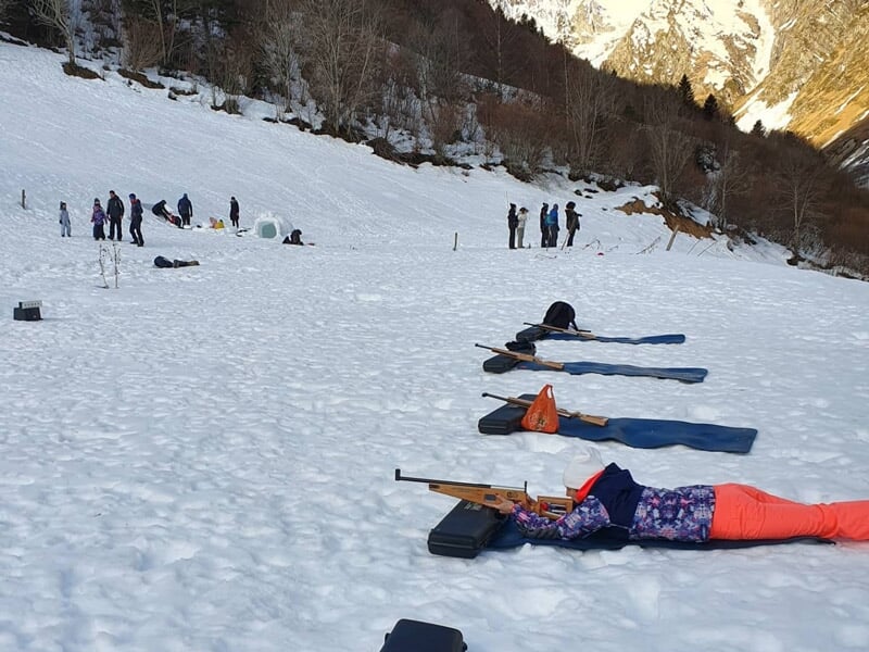 Personnes allongées sur la neige en position de tir avec des carabines, dans un environnement montagneux.