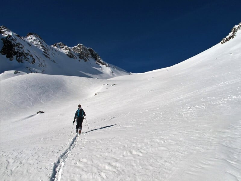 Personne seule marchant dans une vallée enneigée entourée de montagnes sous un ciel bleu profond.