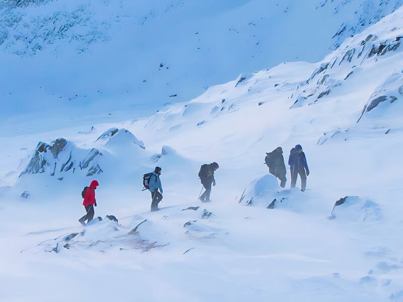 Groupe de randonneurs marchant dans la neige dans un paysage montagneux sous un ciel gris clair.