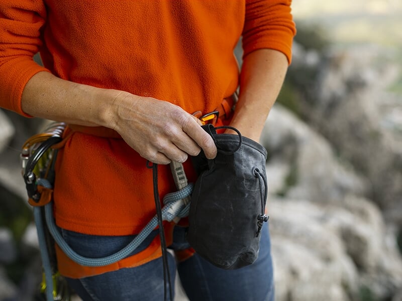 Gros plan sur une personne en tenue d’escalade préparant son sac à magnésie.