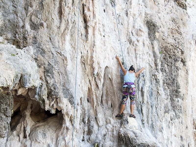 Escalade sur une paroi calcaire claire, une femme grimpe équipée d’un harnais et d’une corde.