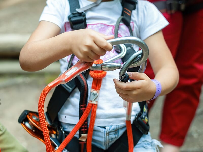 Enfant équipé d’un baudrier manipulant un mousqueton et une corde d’assurage.