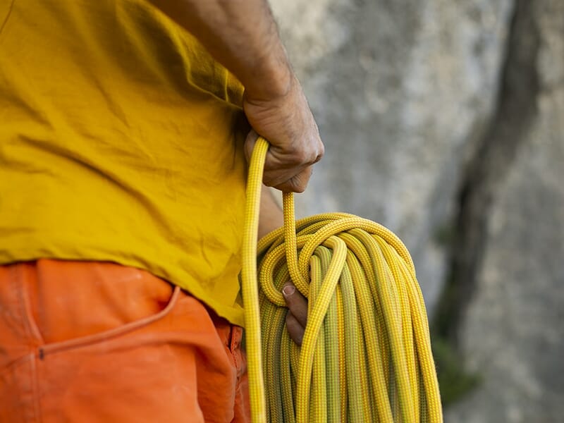 Homme en tenue d’escalade tenant une corde jaune soigneusement enroulée.
