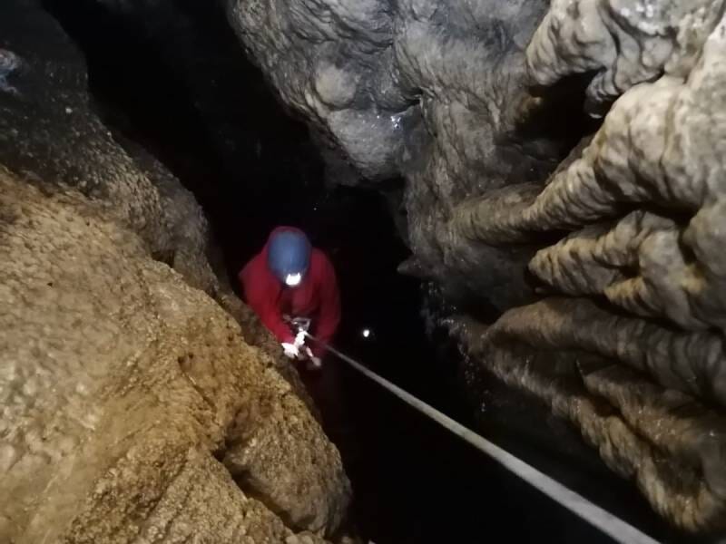 Une personne habillée en rouge descend en rappel dans une grotte.