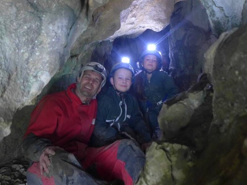 Un guide et deux enfants en tenue de spéléologie prennent la pose dans une grotte.