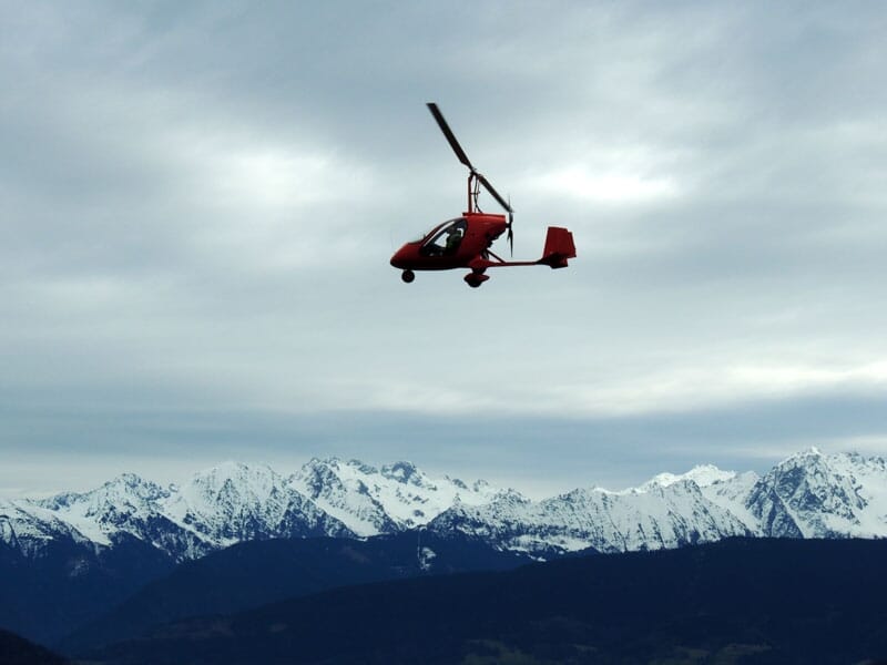 un ULM autogire en plein vol avec la chaîne des alpes en arrière plan