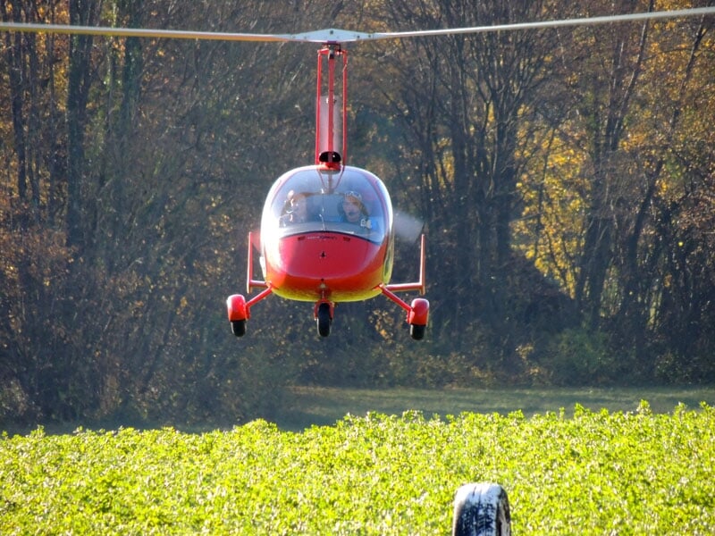 un gyrocoptère rouge survol un champ vert