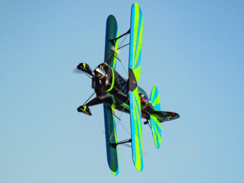Avion de voltige biplan vert et bleu en vol incliné avec un ciel bleu clair en arrière-plan