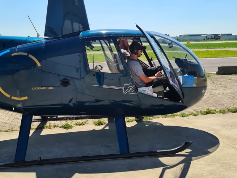 Un homme assis dans le cockpit d'un hélicoptère bleu stationné sur l'aérodrome de Reims Prunay.