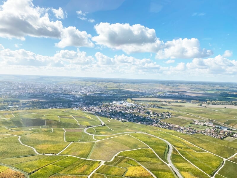 Vue aérienne d'un paysage champêtre avec des routes sinueuses et un ciel bleu parsemé de nuages.