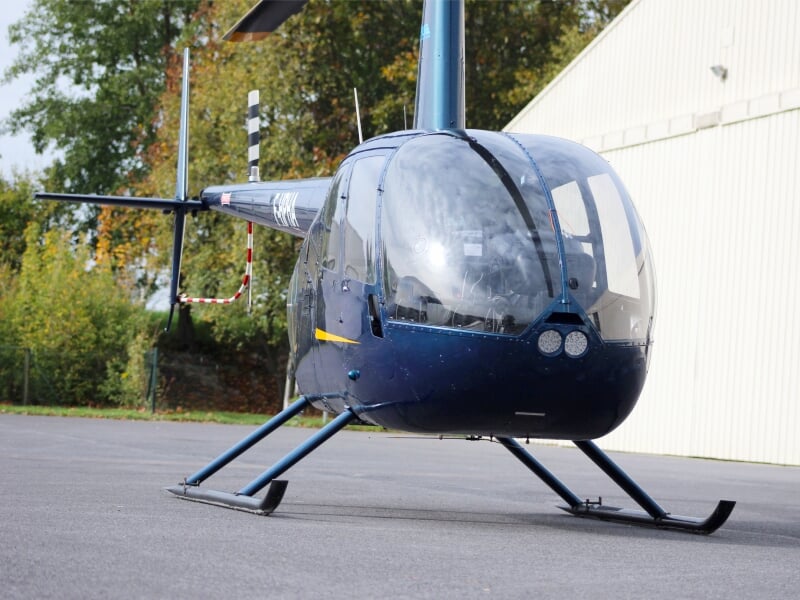 Hélicoptère bleu foncé posé au sol devant un hangar, prêt pour un vol ou une démonstration.