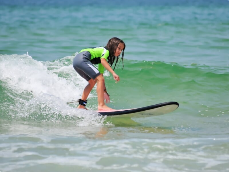 Jeune fille en combinaison de surf verte et noire chevauchant une petite vague sur une planche de surf dans l'océan.