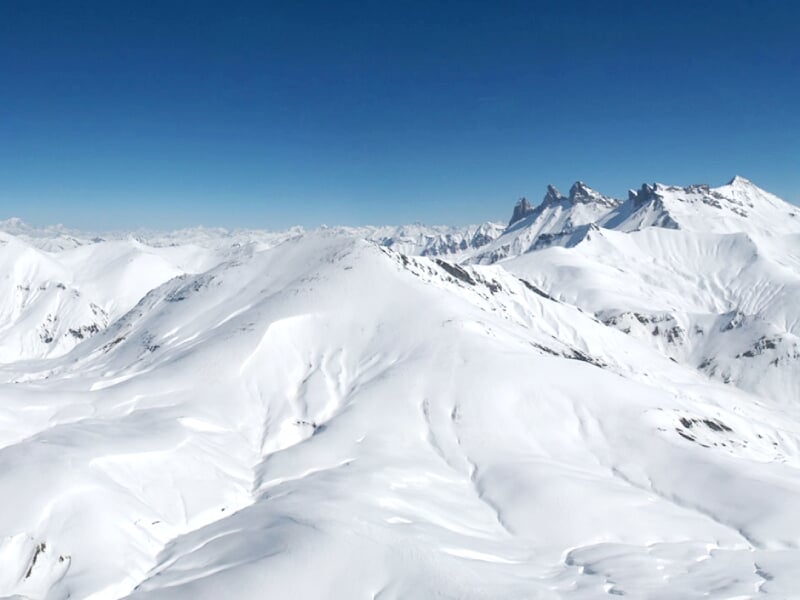 Paysage de montagnes enneigées sous un ciel bleu, avec des sommets arrondis et une atmosphère paisible.