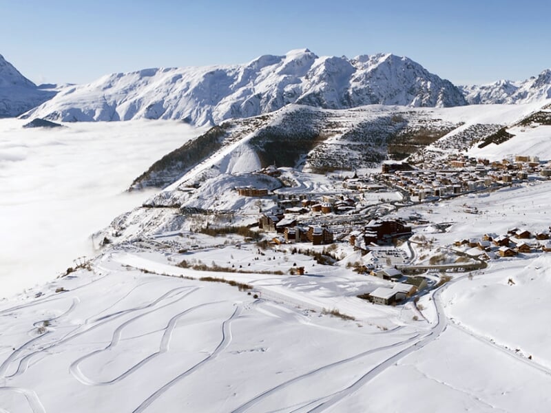 Station de ski en hiver avec des bâtiments entourés de neige et des pistes visibles sur les pentes.