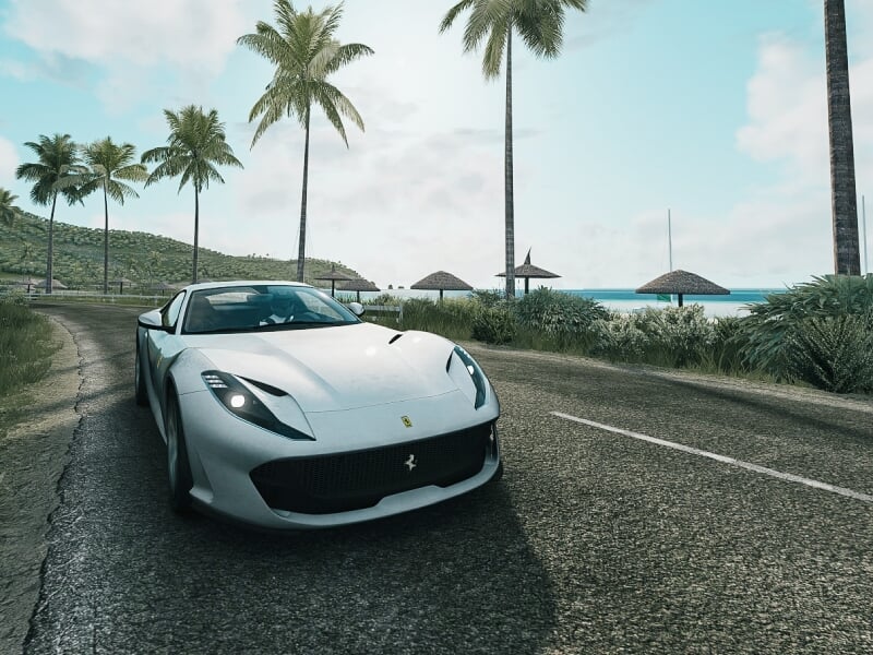 Voiture de sport Ferrari blanche roulant sur une route bordée de palmiers près de la plage, avec un ciel bleu et des parasols en arrière-plan, évoquant une ambiance de luxe et d'évasion
