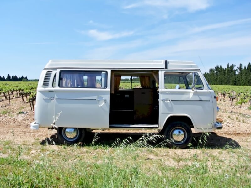 Combi blanc avec porte latérale ouverte stationné dans un champ de vignes sous un ciel bleu clair.