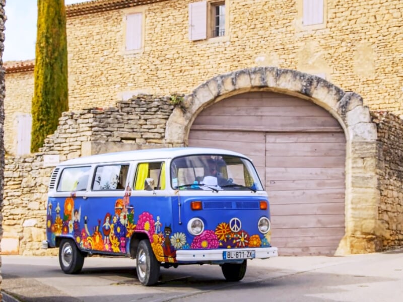 Combi bleu décoré de motifs colorés garé devant un bâtiment ancien en pierre avec une grande porte en bois.