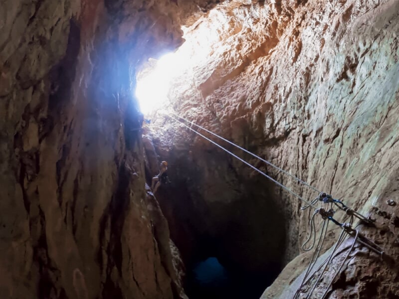 Entrée d'une grotte rocheuse éclairée par la lumière naturelle avec des câbles d'escalade visibles.