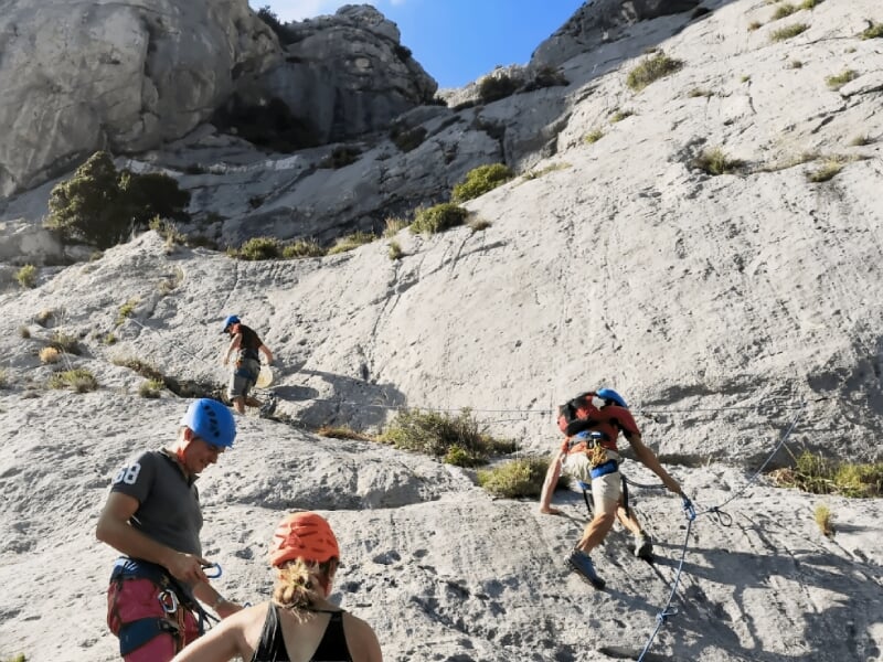 Groupe de grimpeurs équipés de casques bleus progressant sur une paroi rocheuse en terrain escarpé.