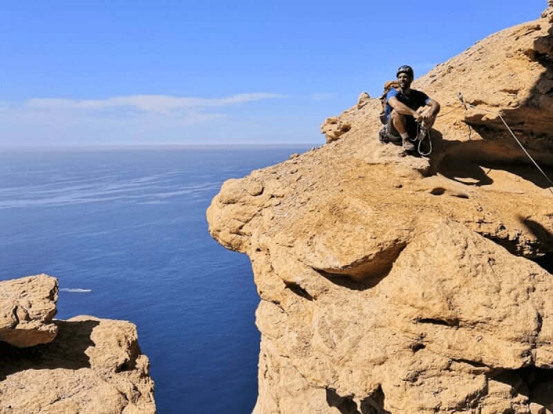 Personne assise sur un rocher surplombant la mer, profitant d'une vue panoramique sur l'océan.