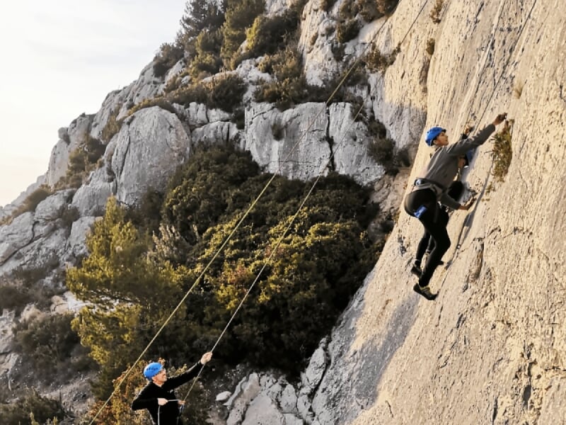 Personne en casque rouge escaladant une falaise rocheuse grise avec concentration et effort.