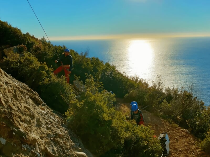 Grimpeur en casque rouge escaladant une falaise rocheuse grise avec des prises naturelles visibles.