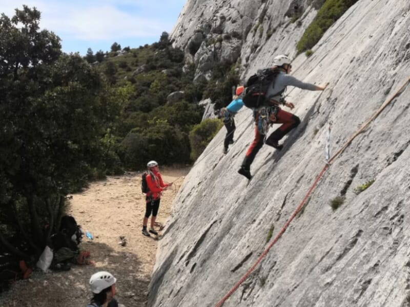 Escalade sur paroi rocheuse, groupe de grimpeurs avec équipement de sécurité, casque et baudrier, paysage de montagne en arrière-plan.