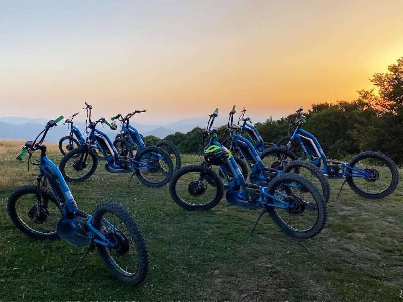 Groupe de trottinettes électriques bleues stationnées sur une colline au coucher du soleil.