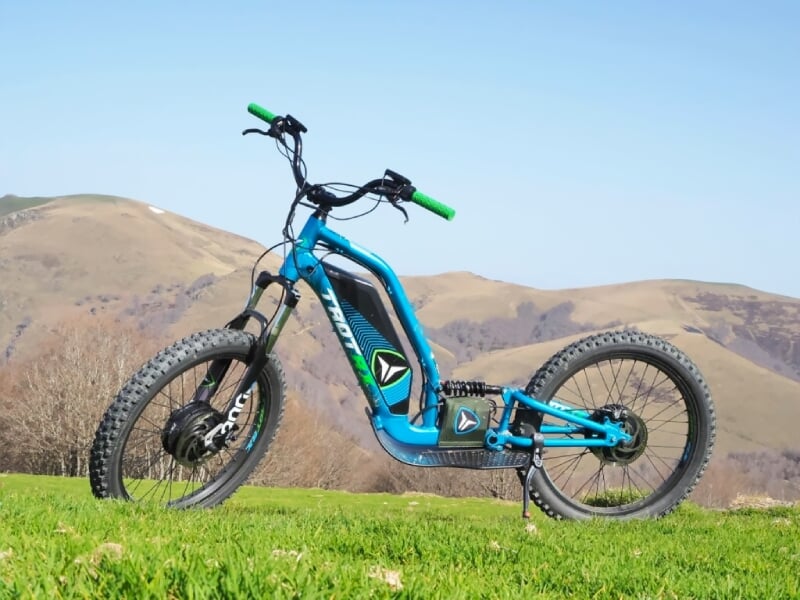 Trottinette électrique bleue posée sur une colline avec des montagnes en arrière-plan sous un ciel clair.