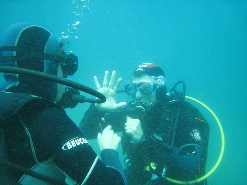 Deux plongeurs sous l'eau communiquent avec la main lors d'un baptême de plongée à l'Estaque.