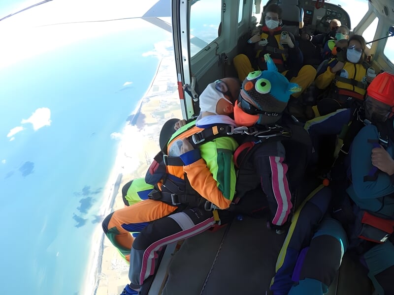 Parachutistes en combinaison colorée assis dans un avion prêt à décoller, avec vue sur la mer et la côte.