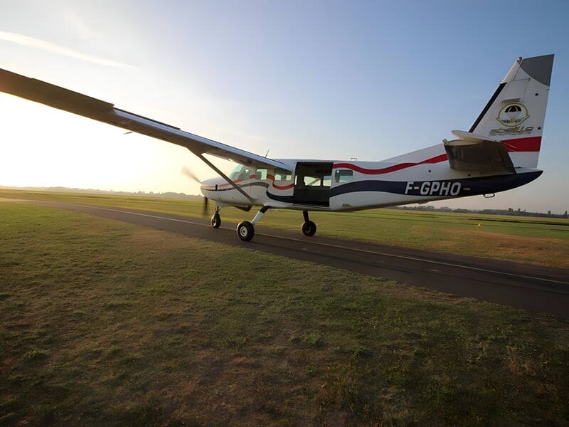 Petit avion blanc avec des bandes rouges et bleues roulant sur une piste d'aéroport au coucher du soleil.