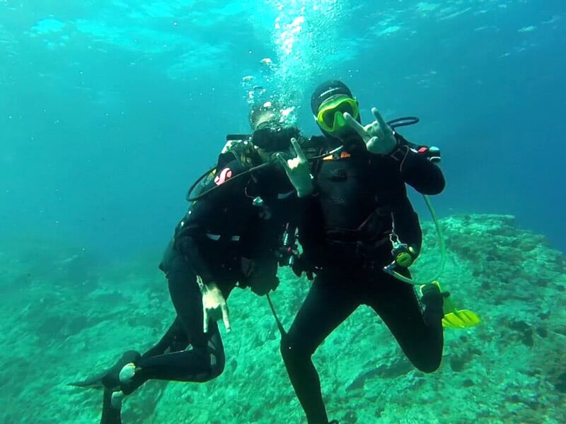 Deux plongeurs sous l'eau posent pour la photo en faisant des signes de la main.
