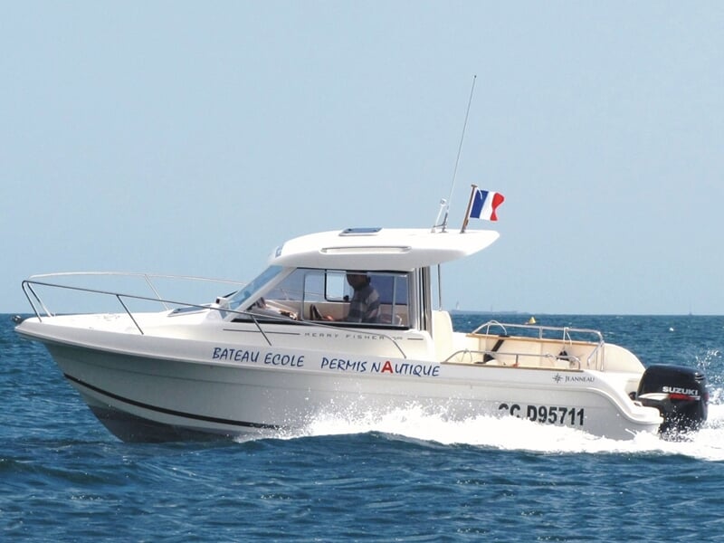 Bateau-école blanc avec drapeau français naviguant sur une mer calme sous un ciel bleu clair.