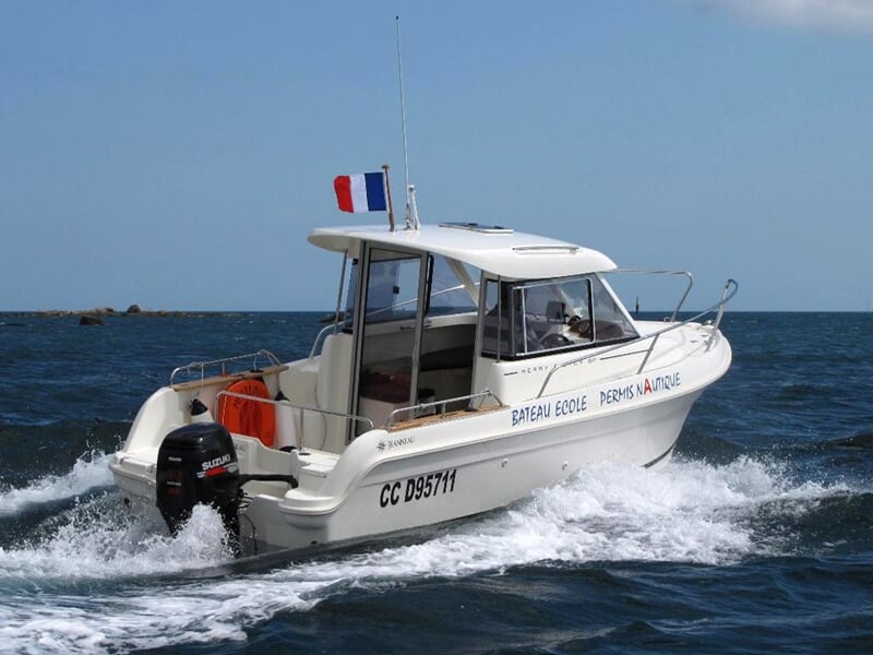 Bateau-école blanc avec moteur hors-bord naviguant sur une mer bleue avec un ciel dégagé.