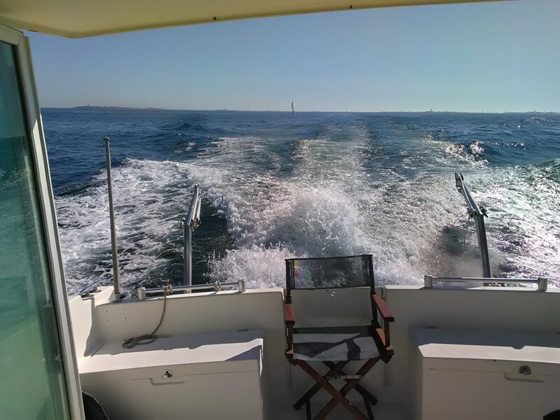 Vue arrière d'un bateau en mer avec une chaise sur le pont et des vagues créées par le déplacement.